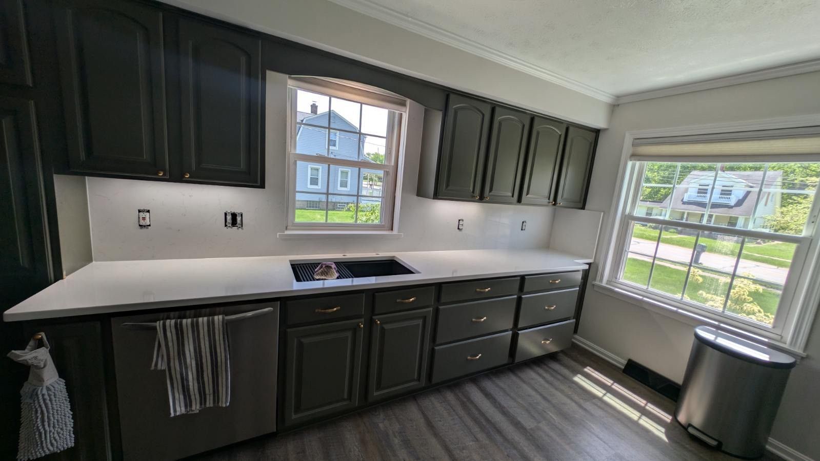 A kitchen with gray cabinets, white countertops, stainless steel appliances, and a large window.