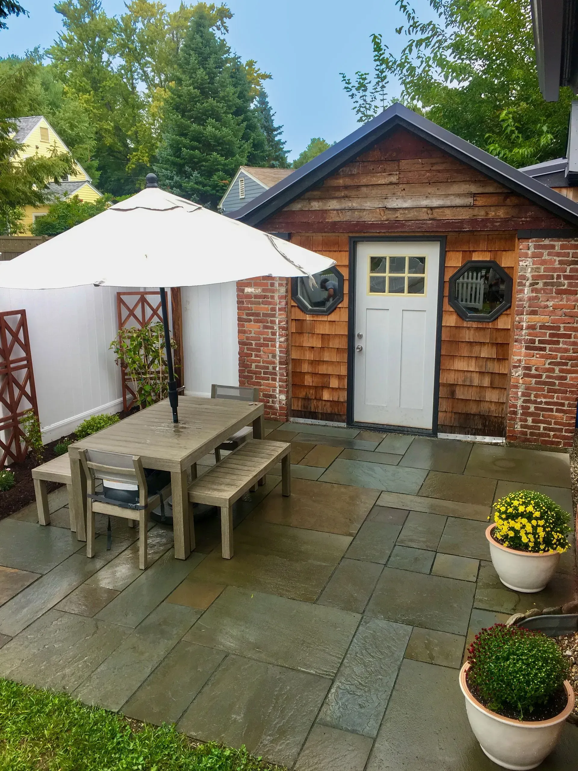 Patio with gray stone, table with umbrella, and wood shed.
