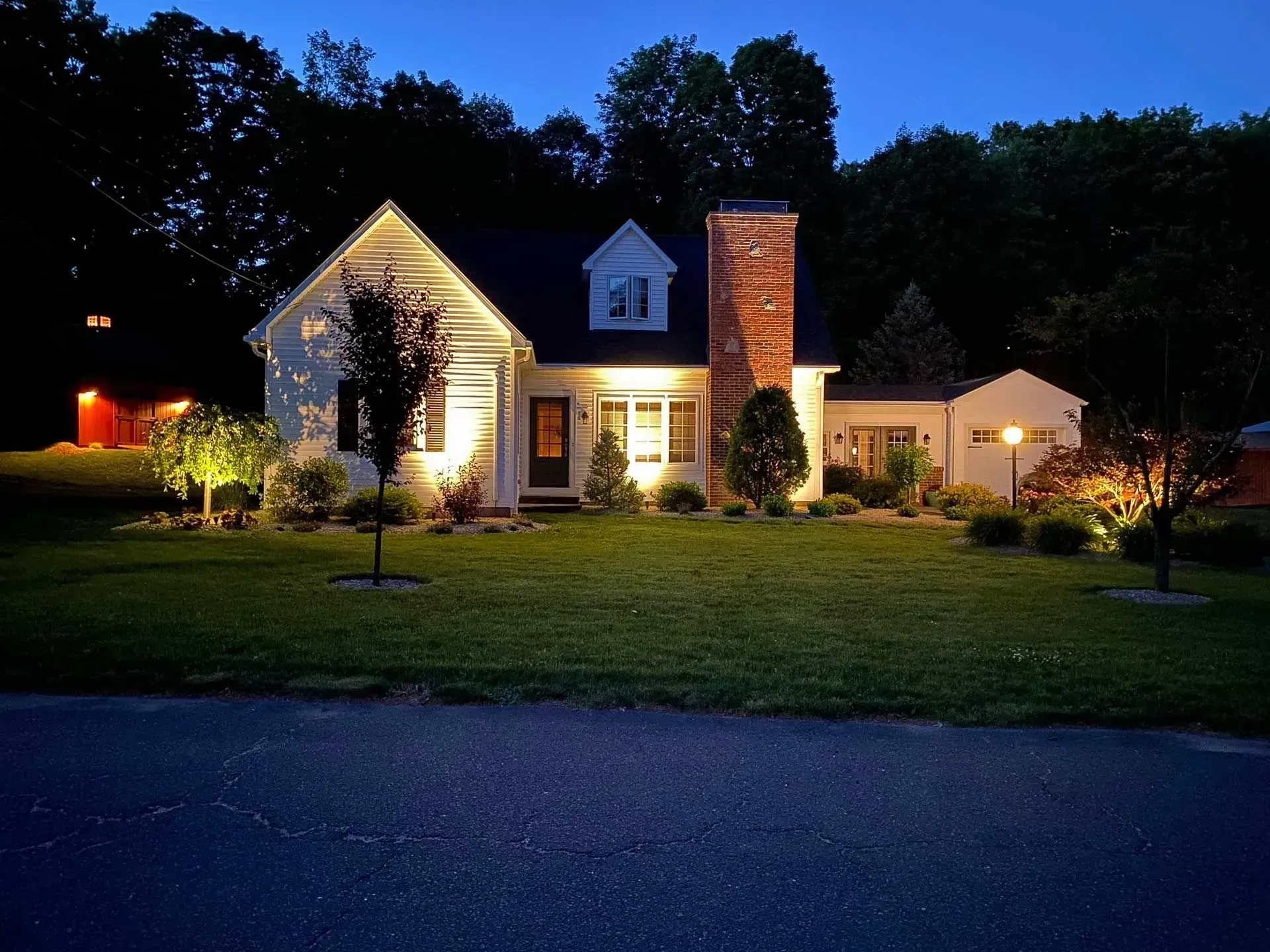 White house at dusk with illuminated landscaping and chimney.
