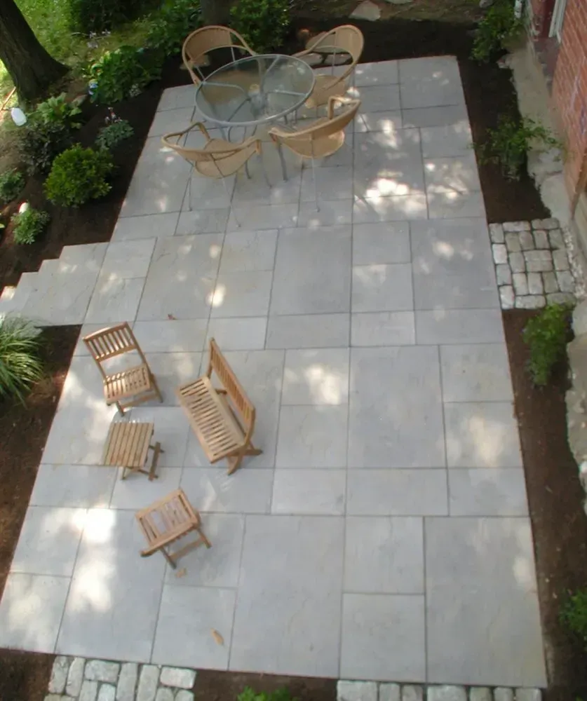 A paved patio with outdoor furniture, surrounded by landscaping, viewed from above.