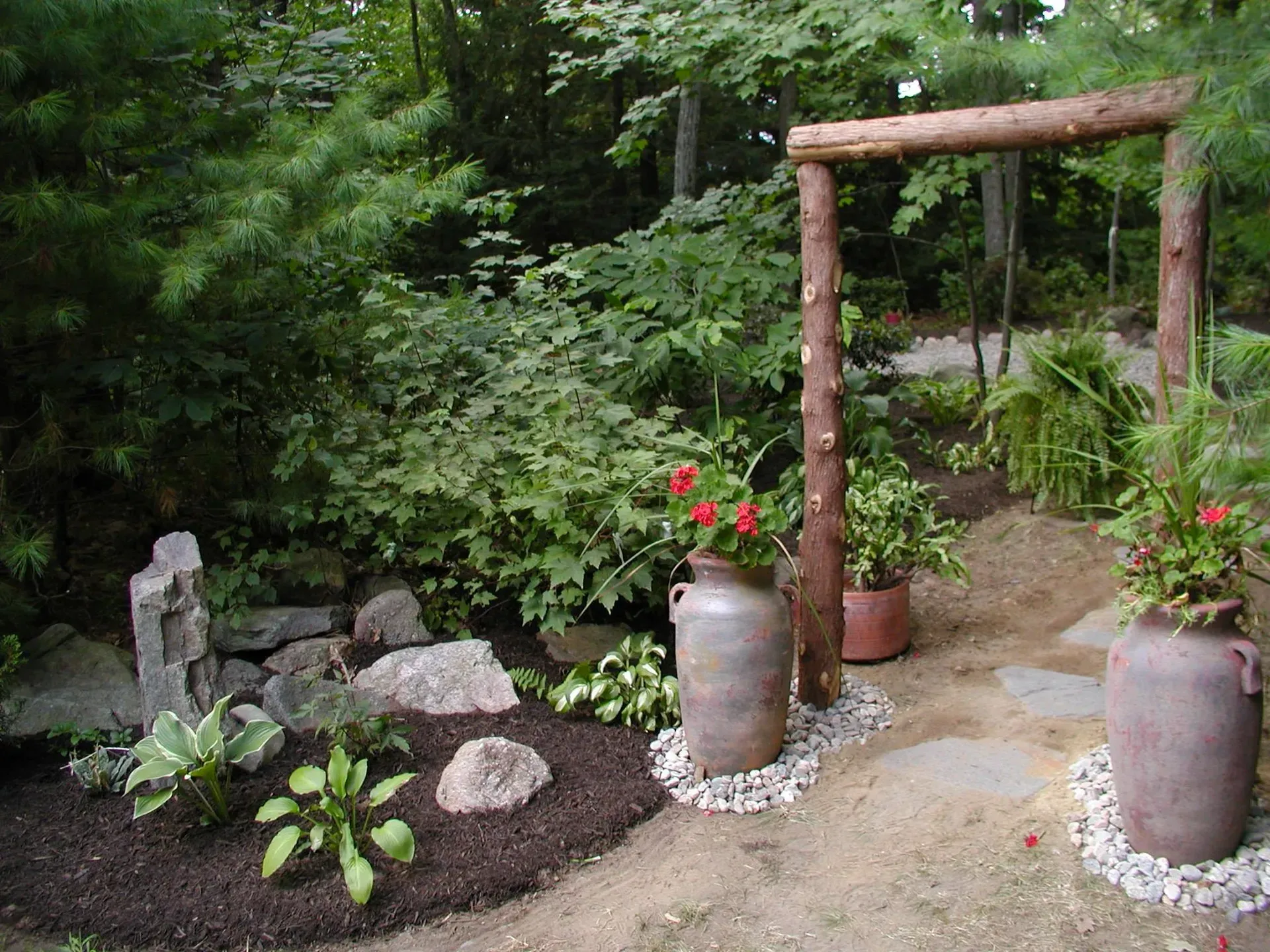 Garden scene: stone path, wooden swing, large planters with red flowers, lush greenery.