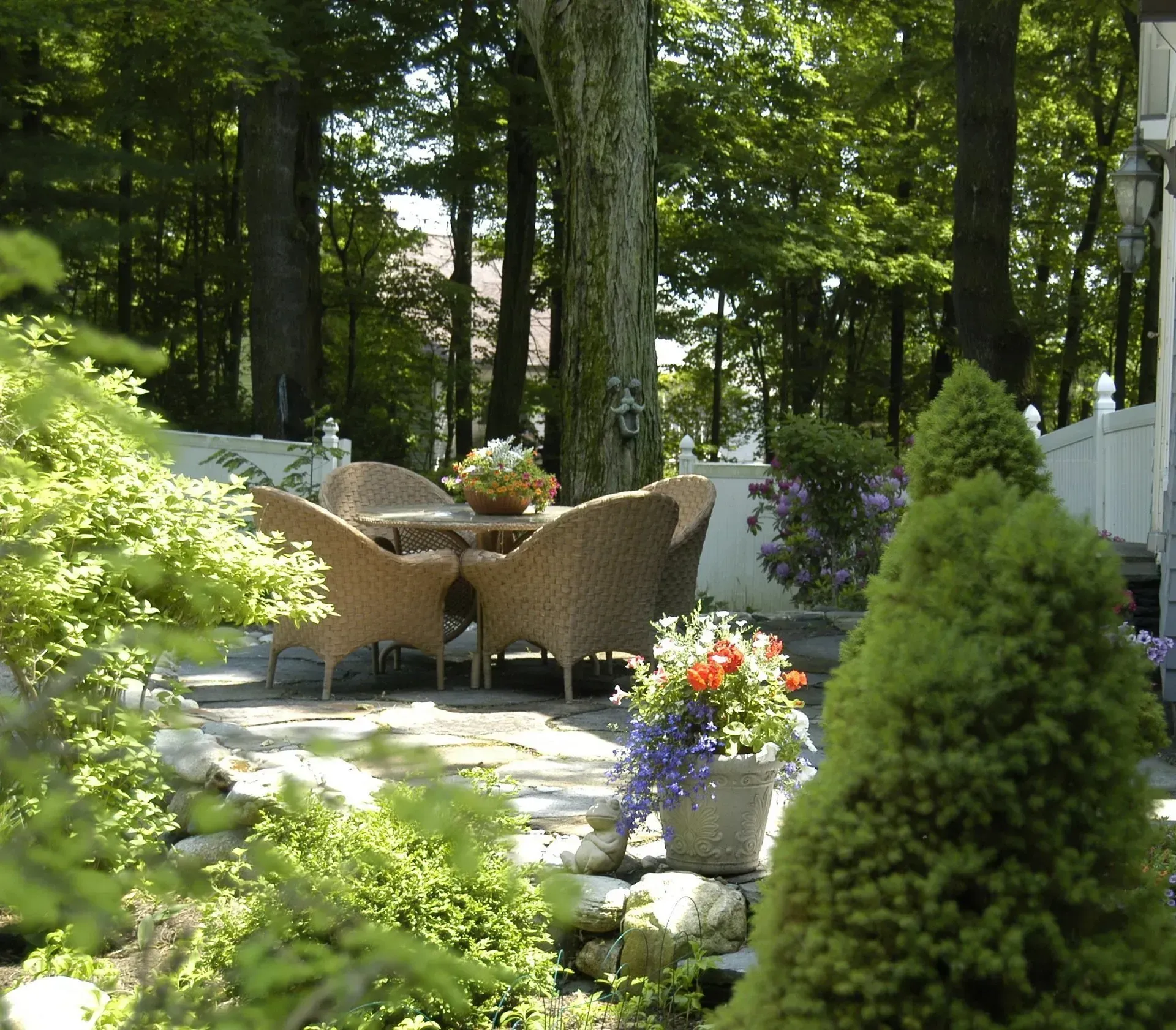 Patio with wicker furniture, surrounded by greenery and trees.