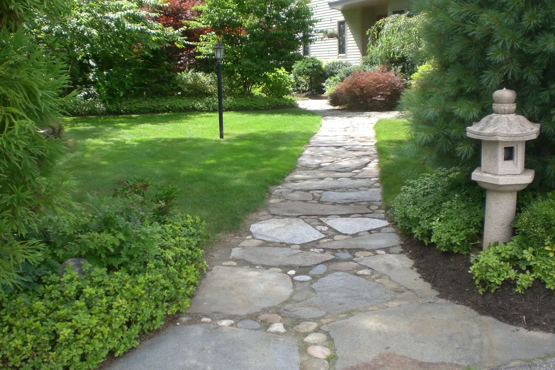 Stone path through a green lawn, garden with bushes and a stone lantern.