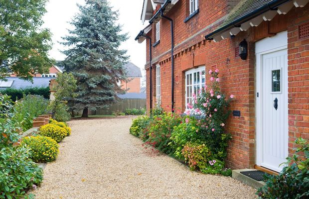 Brick house with gravel driveway and garden, white door, and evergreen trees.