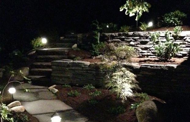 Nighttime landscape with illuminated stone steps, retaining walls, and plants.