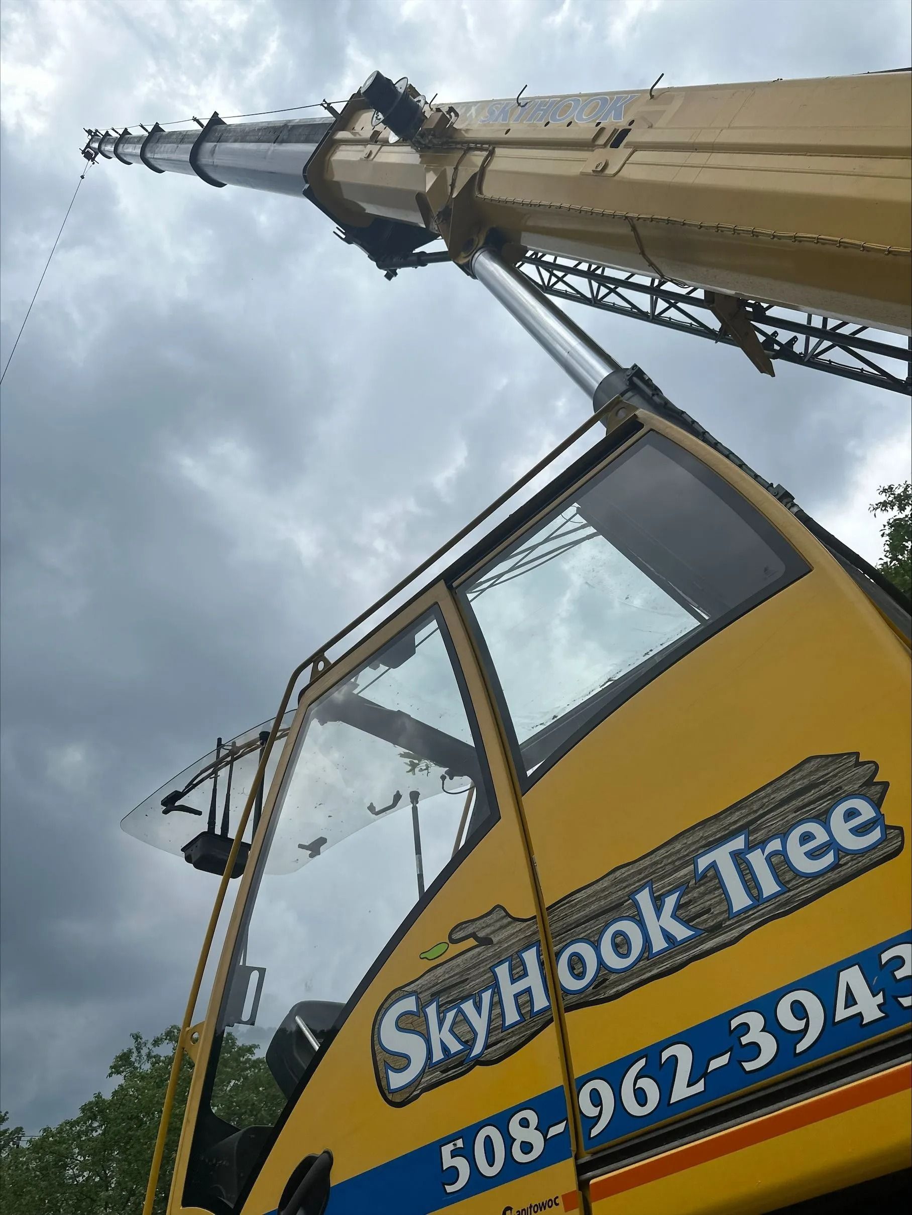 Yellow crane from SkyHook Tree company with boom extended towards a cloudy sky.