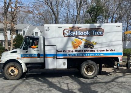 SkyHook Tree service truck parked on a street; white truck with logo, "SkyHook Tree" and service details.
