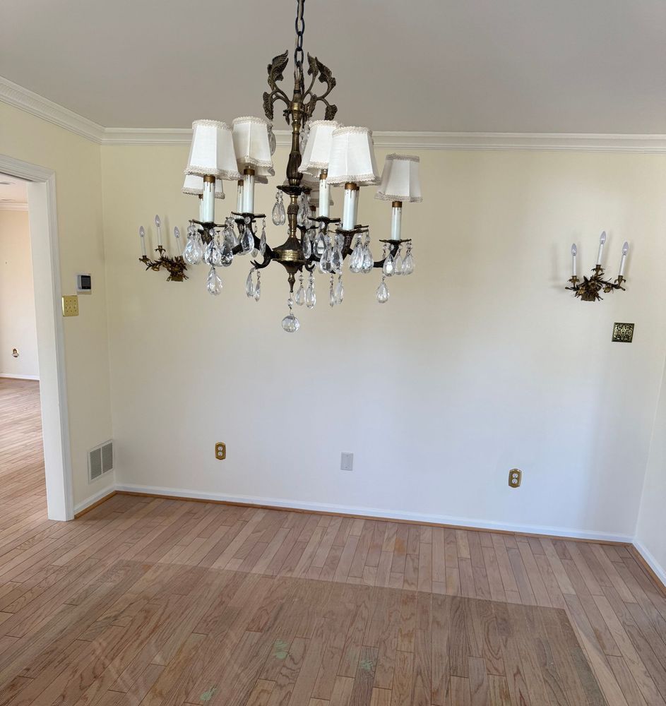 Empty room with light wood floor, off-white walls, chandelier, and sconces.