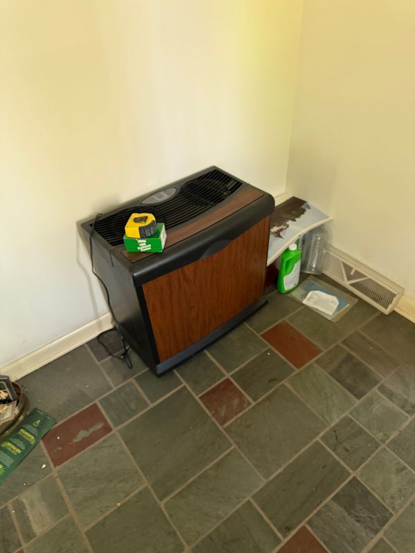 Black and brown heater in a corner, with a tape measure on top, on a tiled floor.