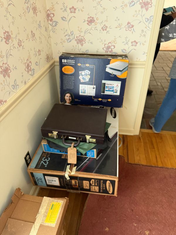 Boxes stacked near a doorway with a briefcase on top. Floral wallpaper in background.