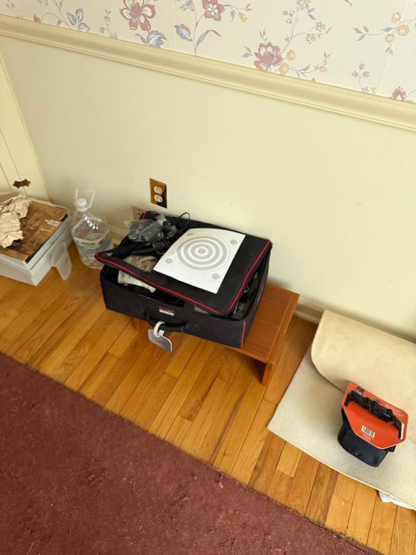 Suitcase with equipment on a wooden step, near a wall with outlet, water bottle, and tool box.