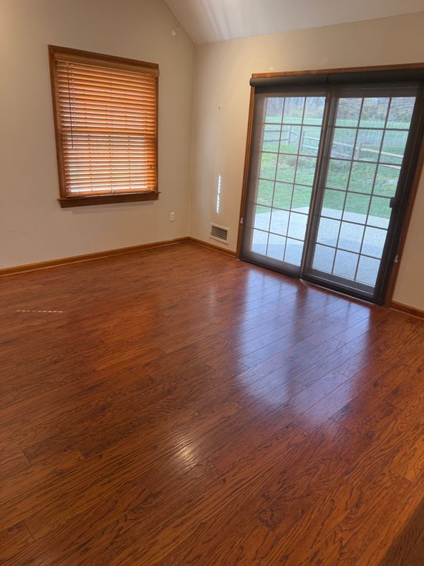 Empty room with hardwood floors, a window with blinds, and a sliding glass door.