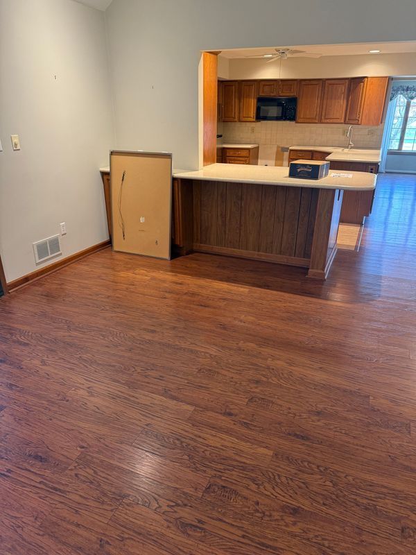 A room with wood flooring, a kitchen, and a bar area with a cardboard box.