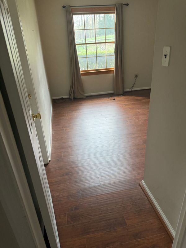 Empty room with wood-look flooring, a window with curtains, and a partially open closet door.