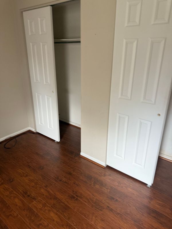 Empty room with open closet doors; brown laminate flooring, beige walls, and white closet doors.