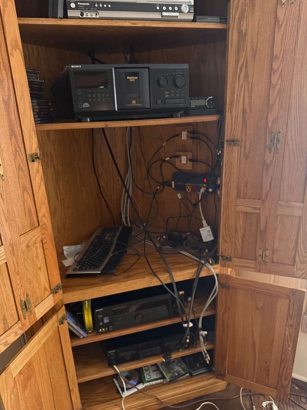Wooden cabinet with open doors, housing audio/visual equipment and tangled wires.