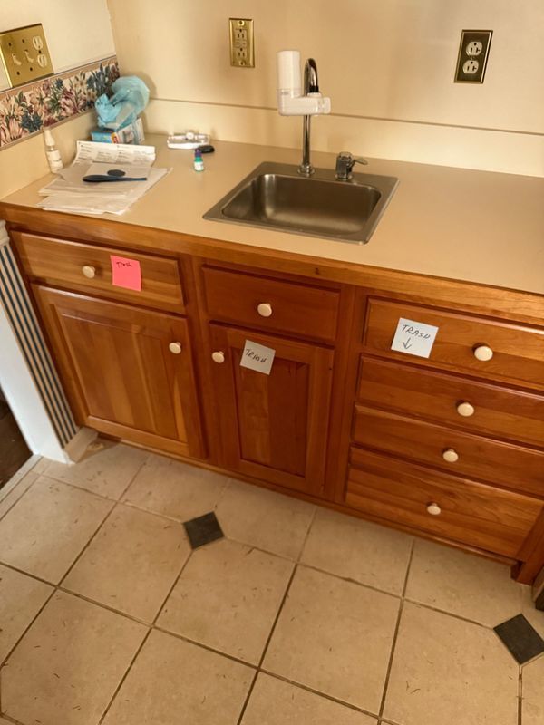 A kitchen cabinet with a sink, drawers, and doors, with beige countertops and tan flooring.
