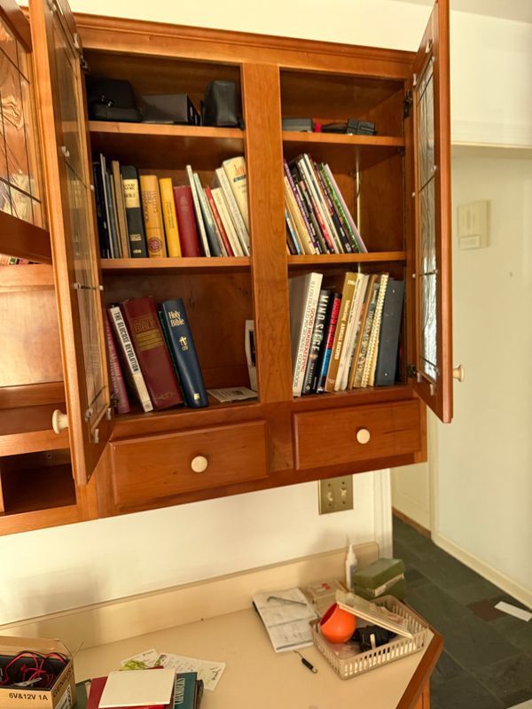 Wooden cabinet with glass doors open, filled with books. White wall and countertop in the setting.