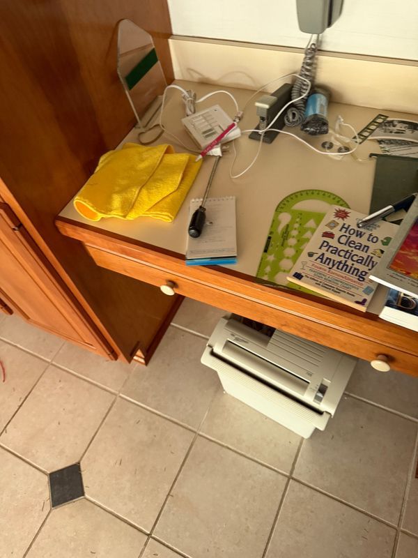 A cluttered desk with cleaning supplies, books, and a printer. Yellow cloth and various tools on the surface.