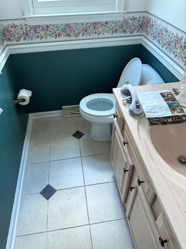 Bathroom with toilet, sink, and vanity. Teal walls, floral wallpaper border, beige tile floor.