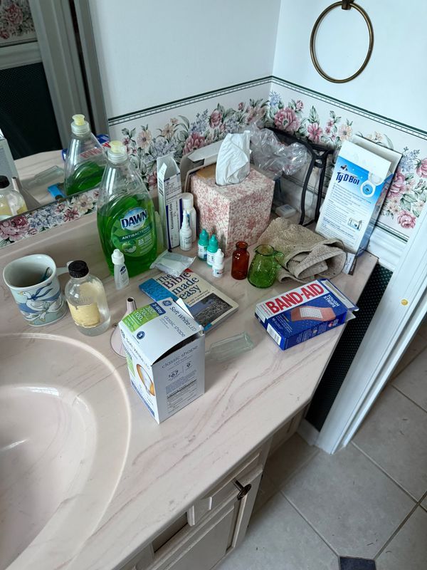 Bathroom counter cluttered with toiletries, bottles, tissues, and a first-aid kit.