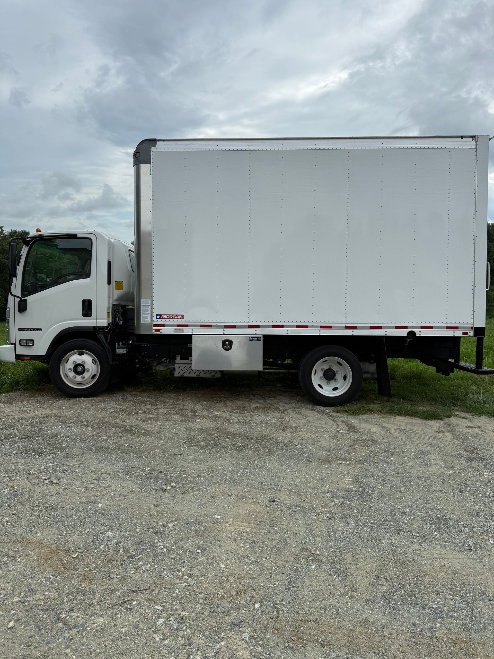 White box truck parked on gravel under a cloudy sky.