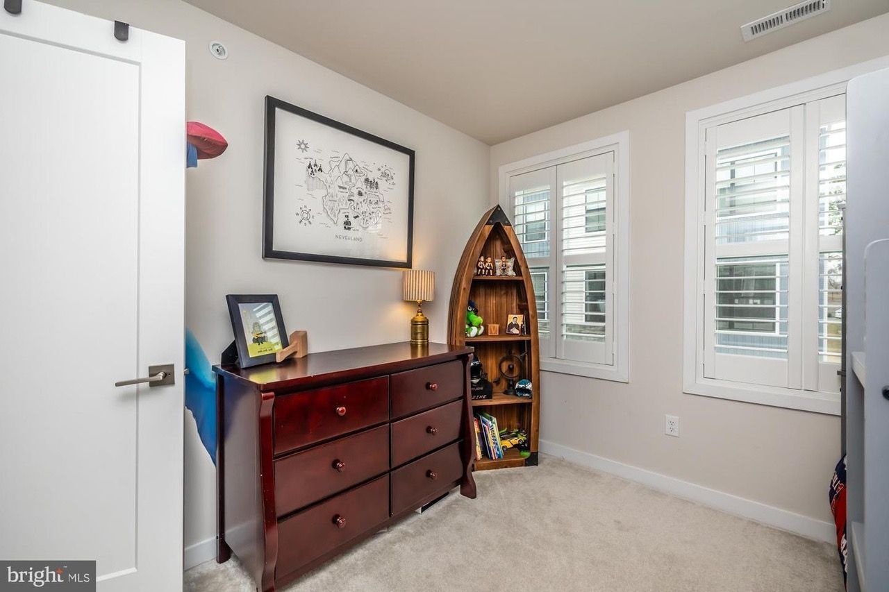 Bedroom with dark wood dresser, bookshelf, two windows, art, and a white door.