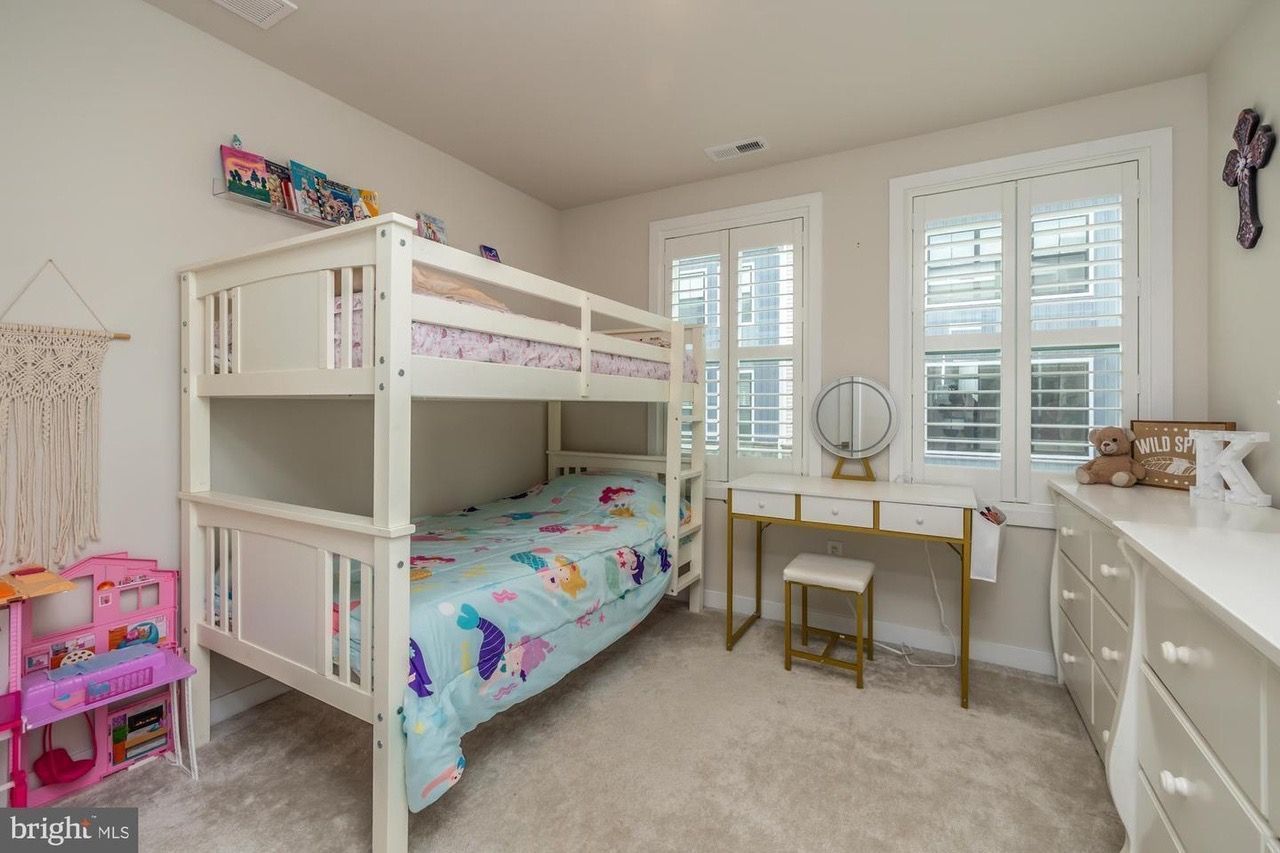 Bedroom with white bunk bed, vanity, and dresser; light walls and carpet.