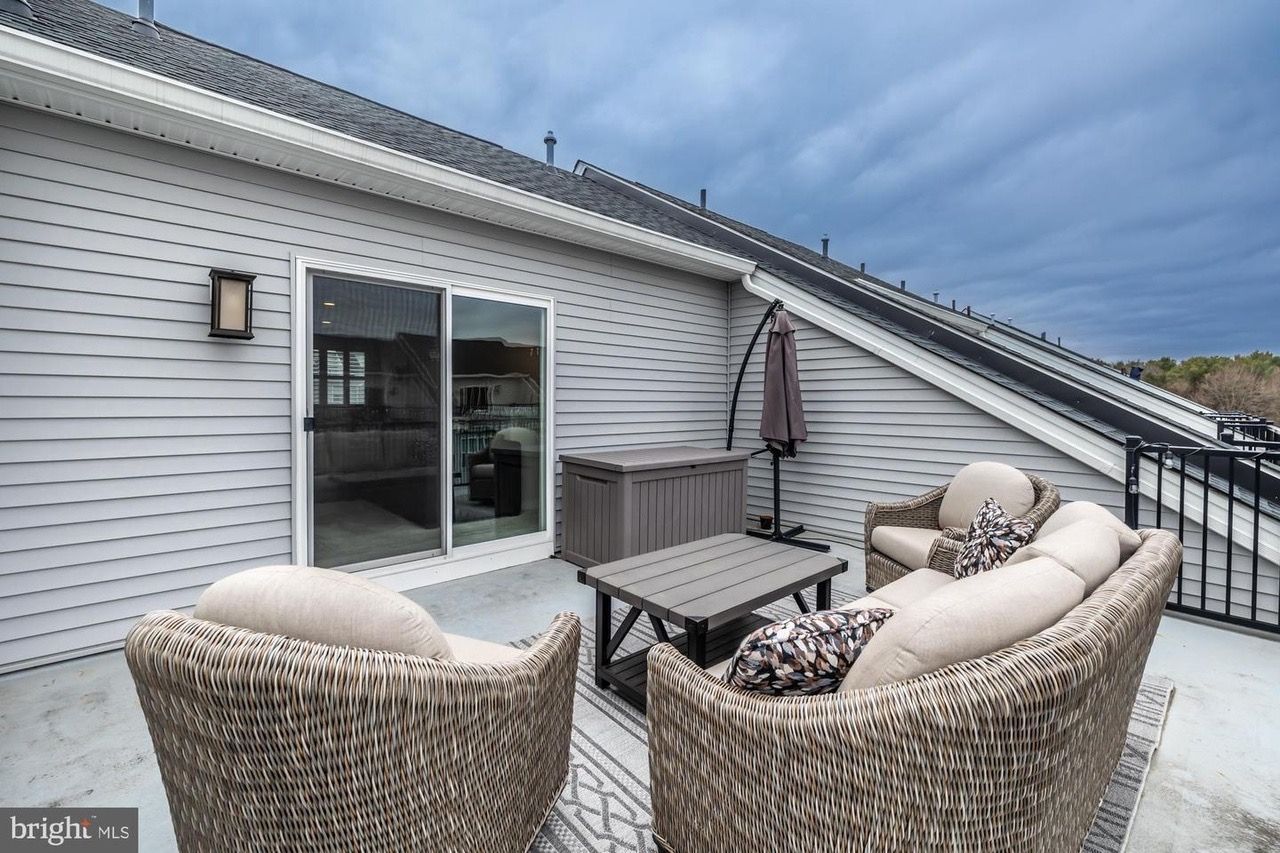 Rooftop patio with wicker furniture, sliding glass door, and a gray, cloudy sky.