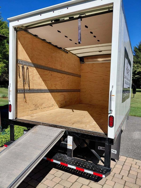 Empty white moving truck with ramp extended, parked outdoors.
