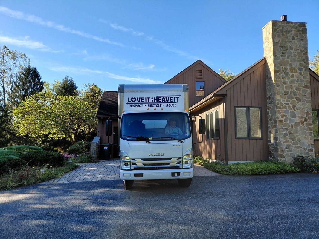 White moving truck in a driveway in front of a brown house. Blue sky with a chimney.