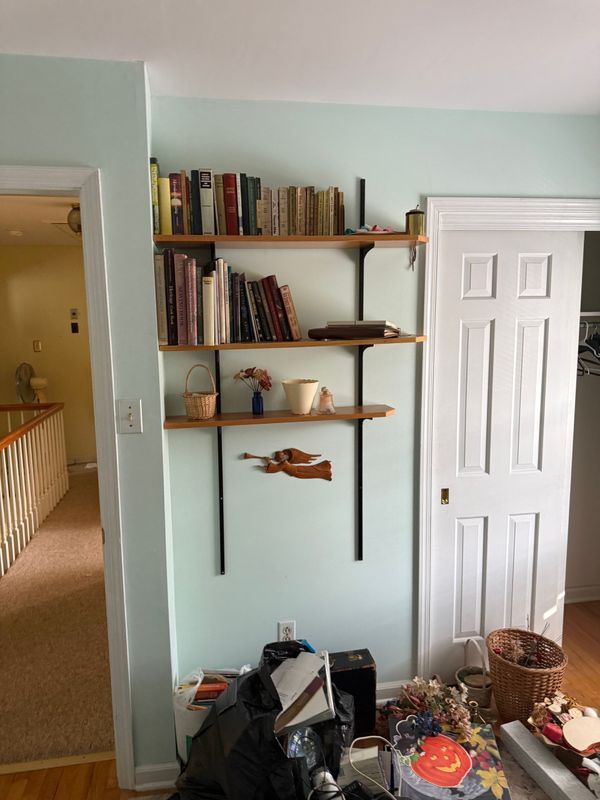Bookshelves with books on a light green wall next to a white door. A cluttered floor in front.