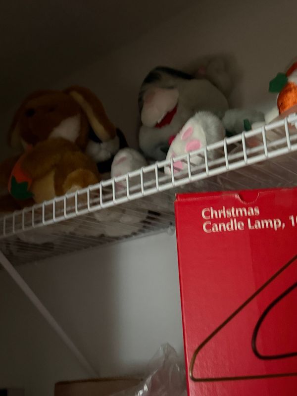 Stuffed animals on a wire shelf above a red Christmas Candle Lamp box.