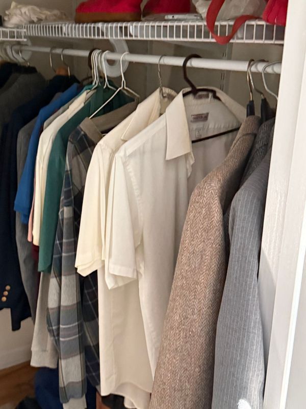 A closet with clothes hanging on a rod. Shirts and jackets in various colors, including green, white, and gray.