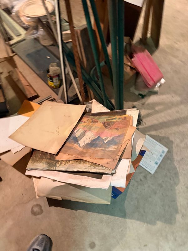 Pile of old papers and books on a concrete floor, with a colorful mountain illustration visible.