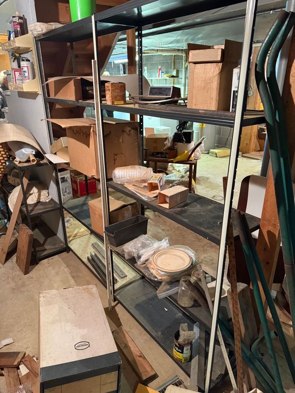 Metal shelving unit in a cluttered workshop holding boxes and various objects.