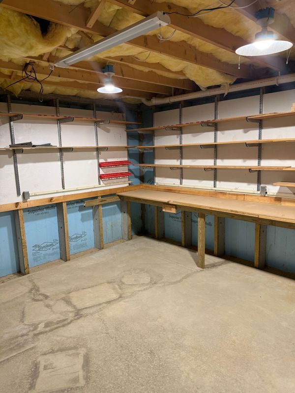 Workshop with built-in wooden shelves and a workbench. Insulation and fluorescent lights are visible.