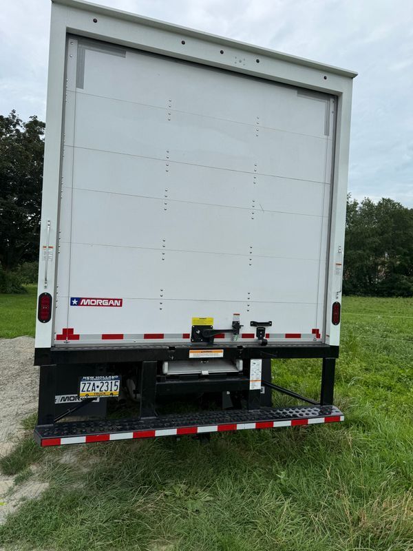 White box truck with a lift gate, parked on grass.