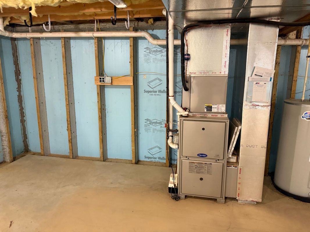 Basement with unfinished walls, blue insulation, furnace, water heater, and concrete floor.