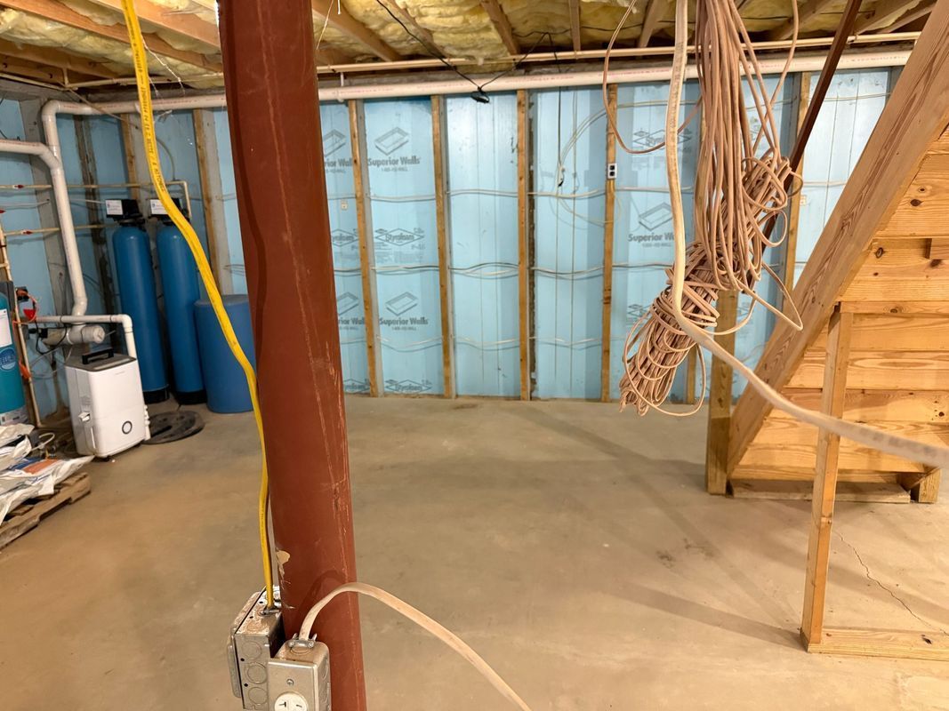 Basement interior with blue insulated walls, support beam, electrical outlets, and water treatment system.