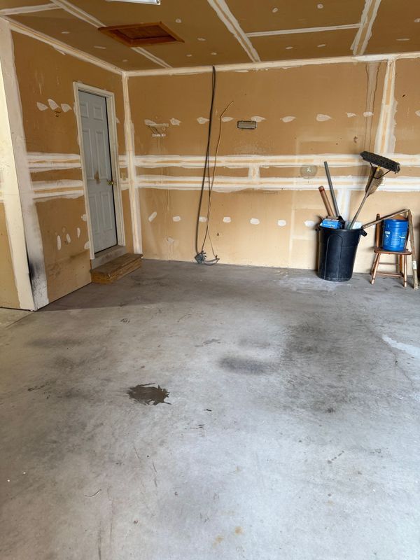 Empty garage with exposed drywall and concrete floor; tools in a bucket.