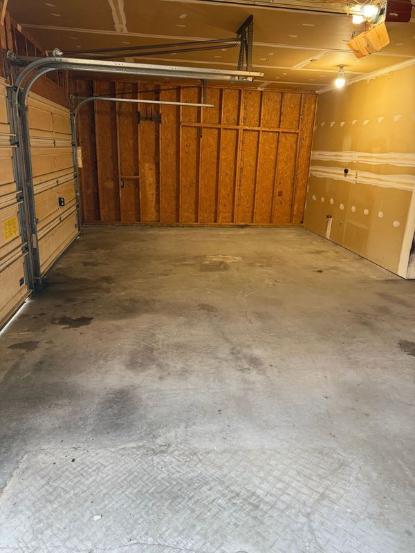 Empty garage with concrete floor and wooden walls, overhead door open.