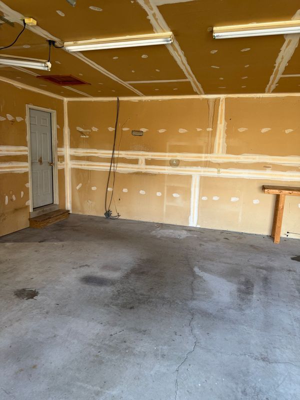 Empty garage with unfinished walls, concrete floor, and fluorescent lights.