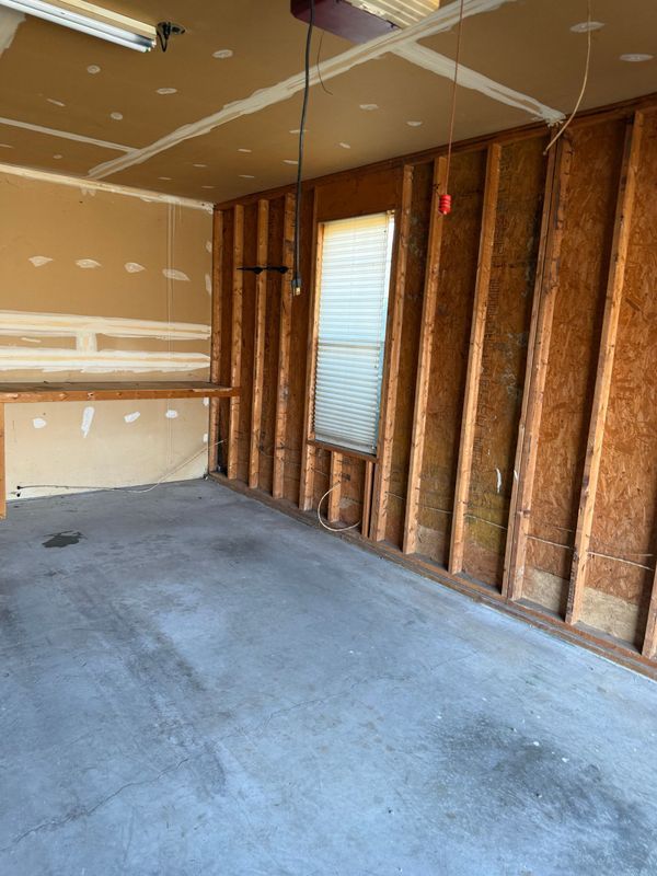 Empty garage interior with exposed studs, window, and unfinished drywall.
