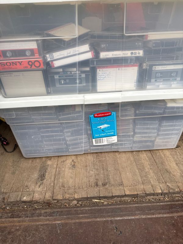 Clear plastic storage bins filled with cassette tapes on a wooden surface.