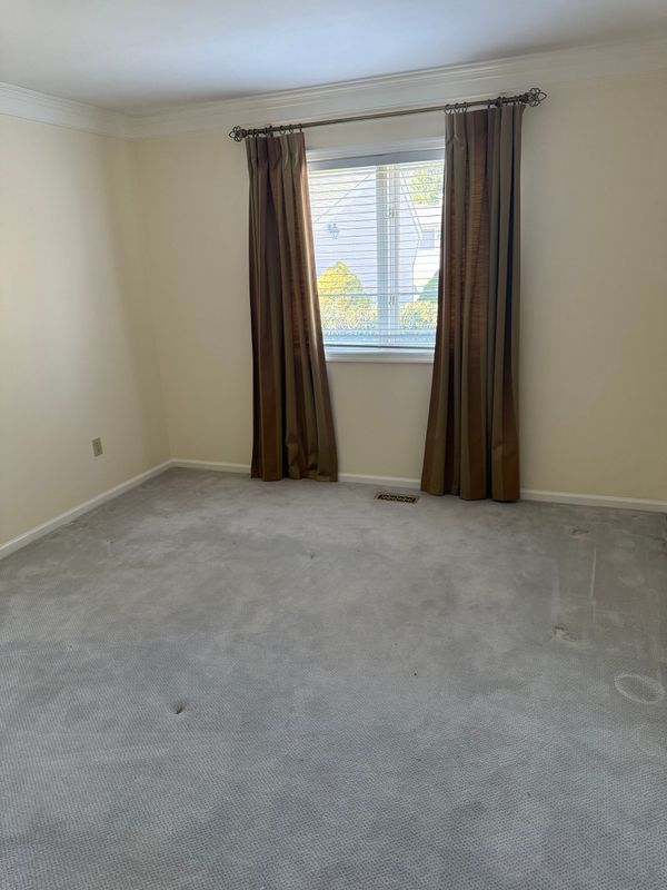 Empty room with beige walls, gray carpet, and a window with brown curtains.
