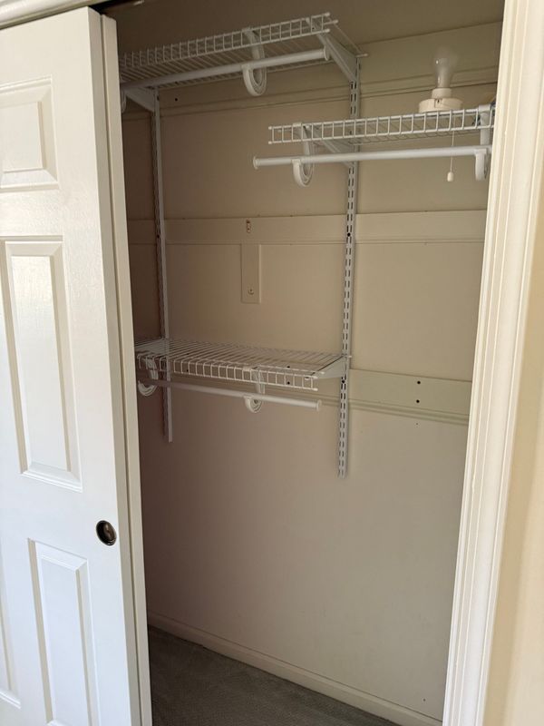 Empty closet with white sliding door, wire shelves and hanging rod. Cream walls.
