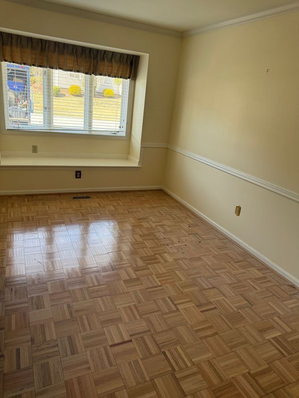 Empty room with parquet floor, window with blinds and valance, and light yellow walls.