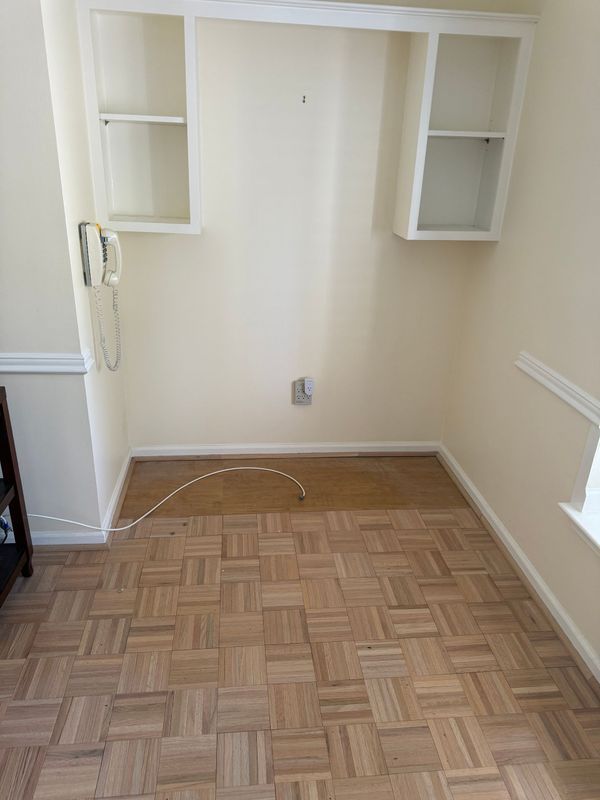 Small room with built-in shelves above a desk area. Parquet flooring and beige walls.