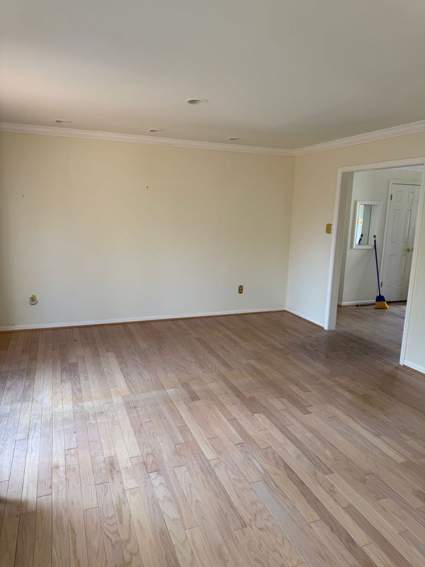 Empty room with wood floors, cream walls, and white trim. Doorway leads to another room.